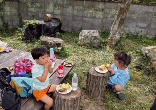 切り株の上でご飯をたべる子どもの写真